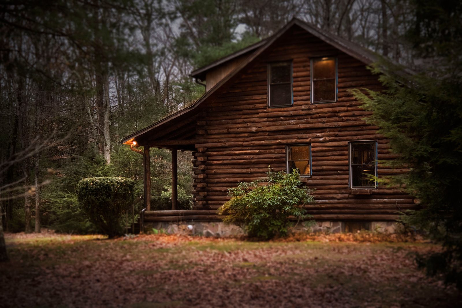 Cozy log cabin lit up at dusk in autumn woods, a Thanksgiving family cabin gathering idea