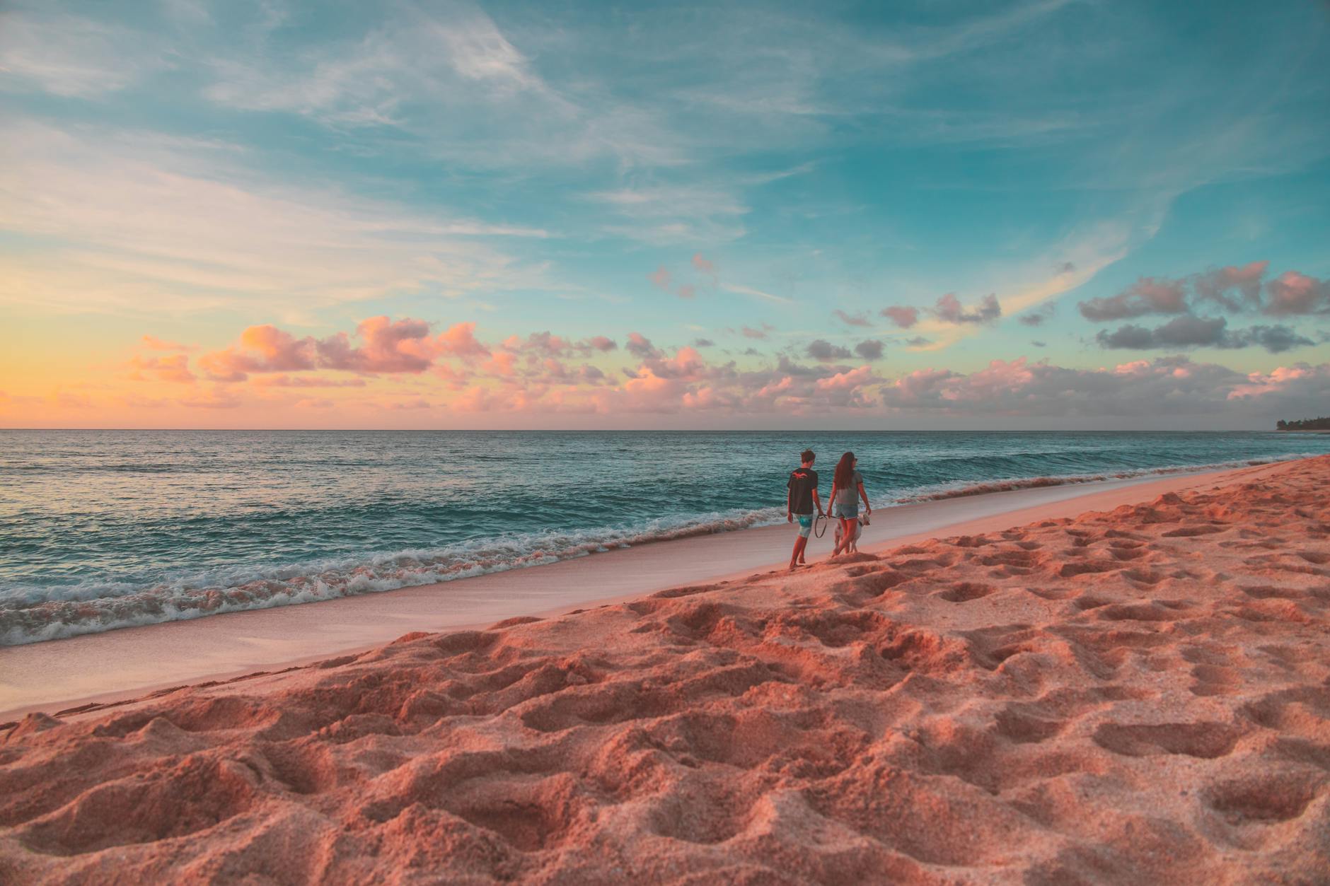 Two people walking along a Hawaiian beach at sunset with calm ocean and colorful sky