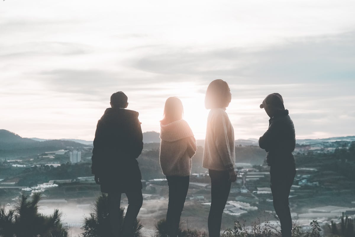 Group of friends standing on a hilltop watching the sunset together