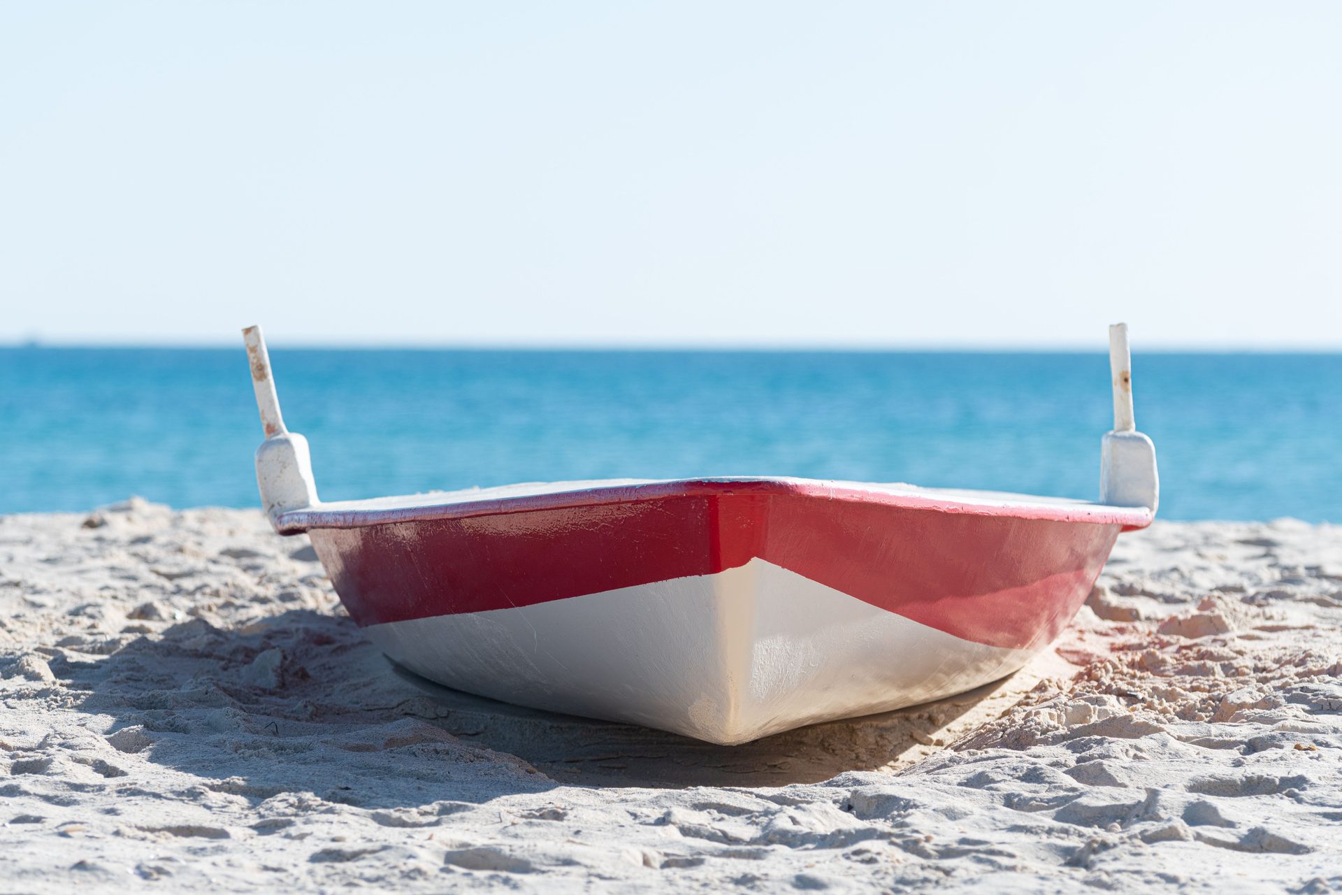 A small red and white boat resting on the sand of a beach in Hammamet, Tunisia, with blue sea behind