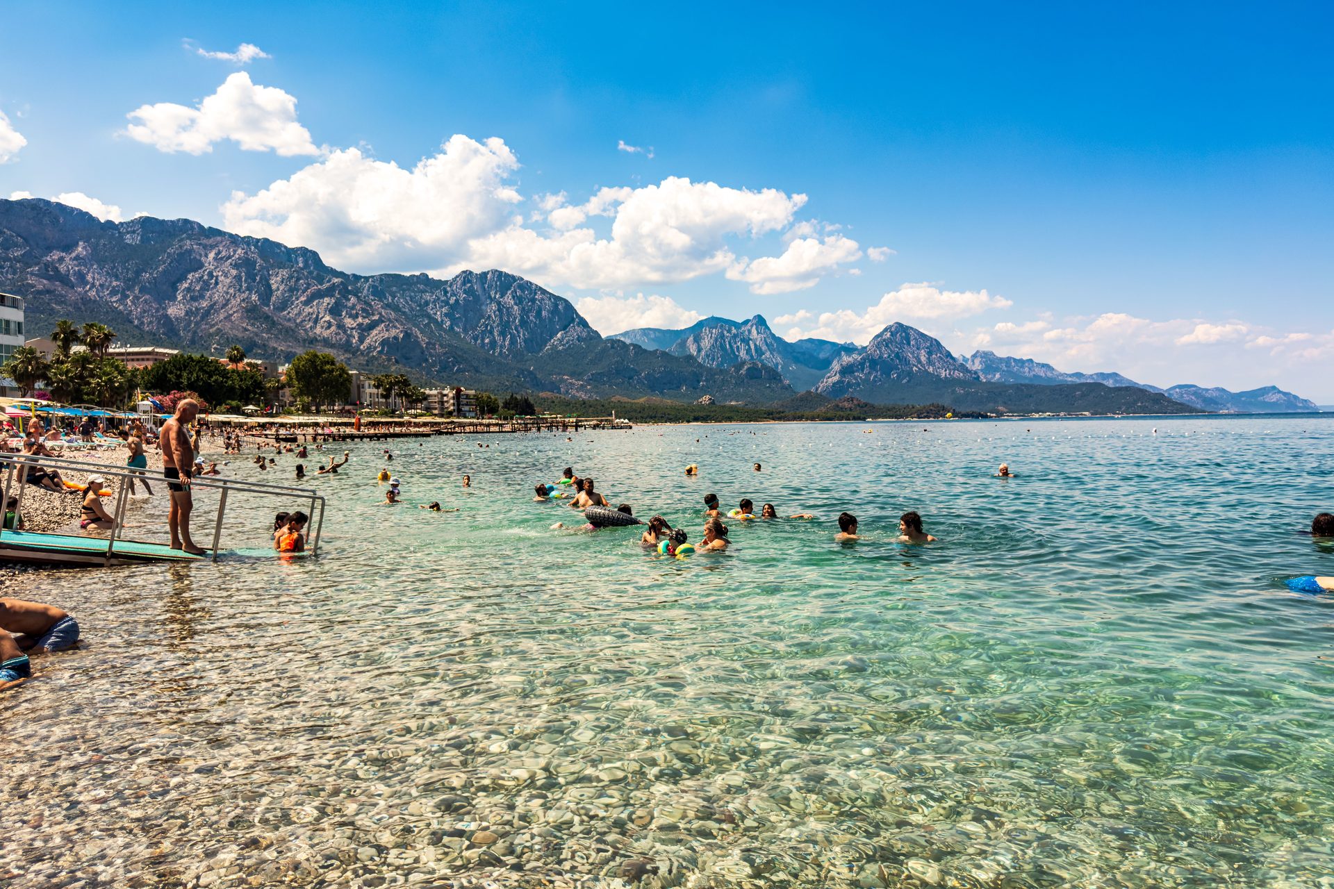 Swimmers in clear water off the pebble beach at Kemer on the Antalya coast, with mountains behind