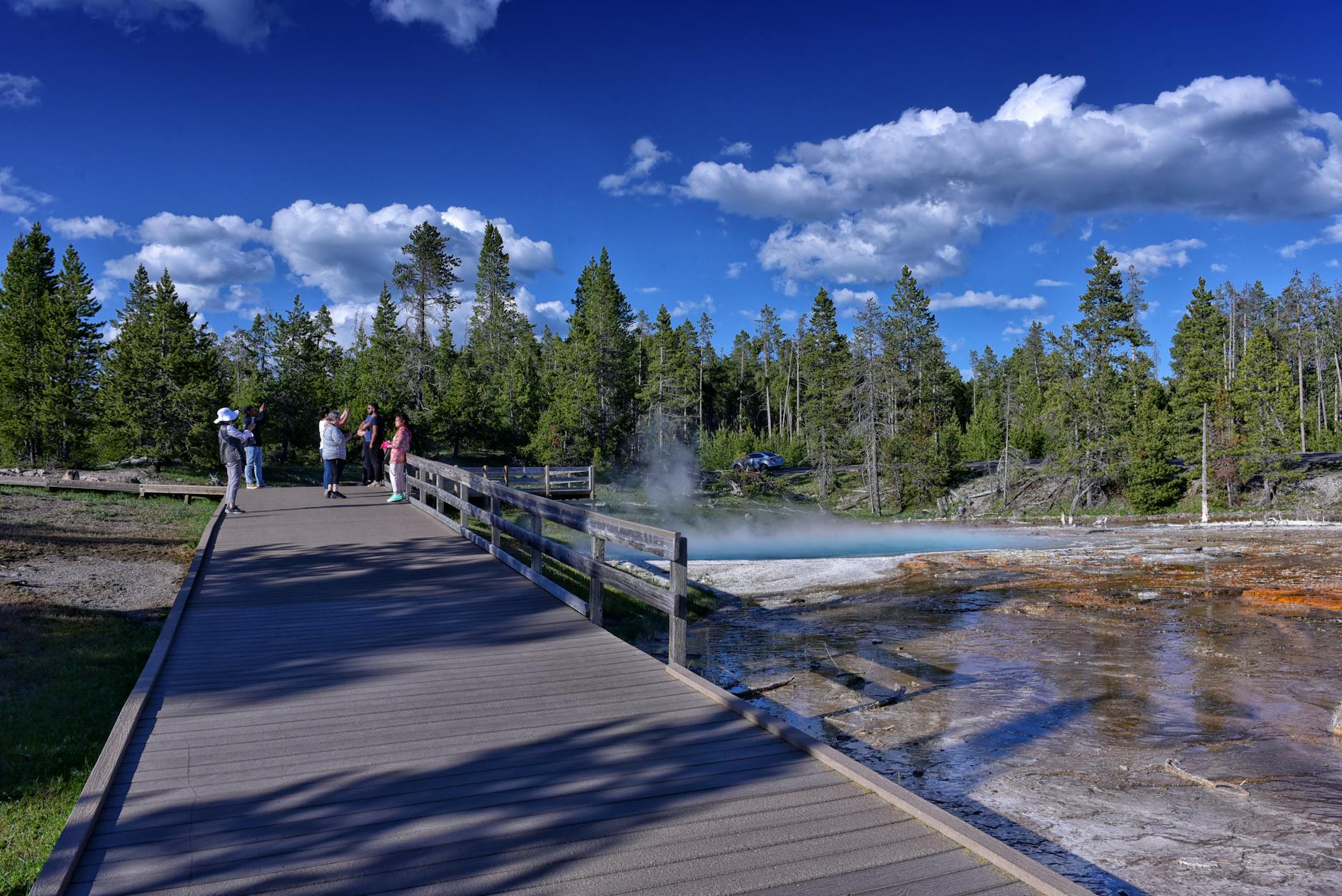 Tourists exploring Yellowstone's geothermal boardwalk under a clear blue sky &mdash; one of the park's free signature experiences